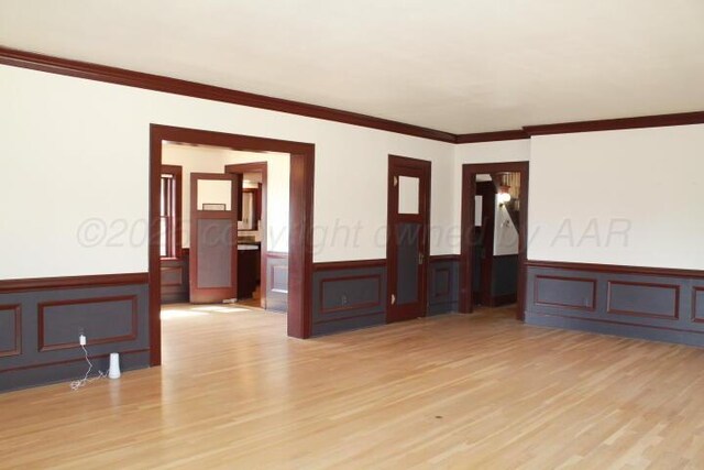 empty room with wainscoting, crown molding, and light wood-style flooring