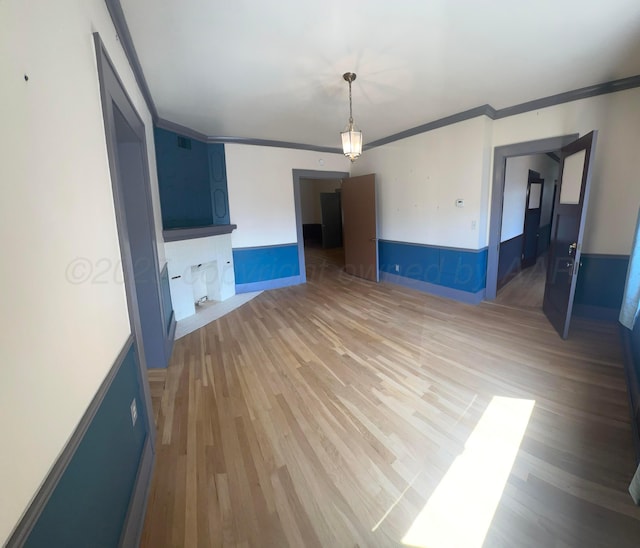 unfurnished living room featuring crown molding, a wainscoted wall, and light wood finished floors