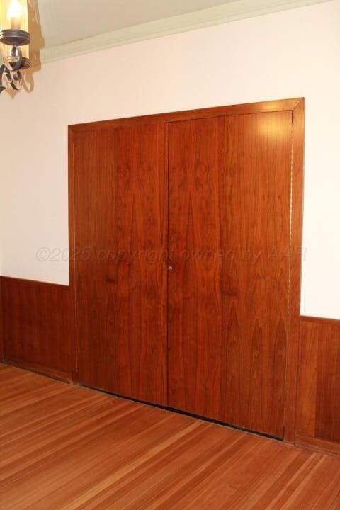 unfurnished bedroom with wooden walls, wood finished floors, ornamental molding, a closet, and a notable chandelier