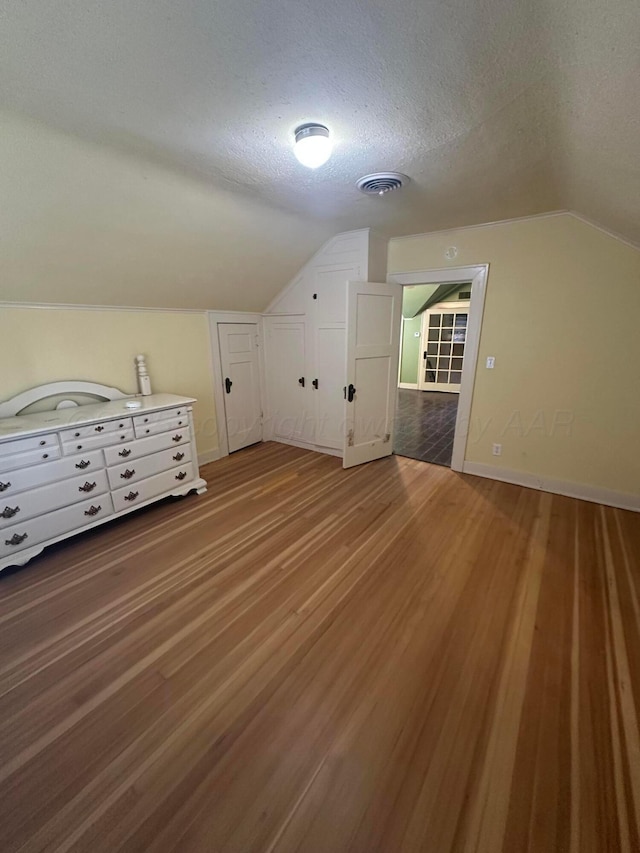 bonus room featuring baseboards, visible vents, lofted ceiling, light wood-style flooring, and a textured ceiling