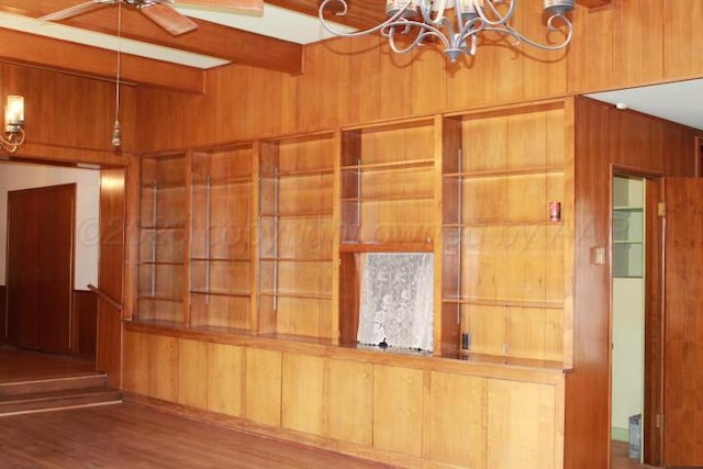 interior space with beam ceiling, wooden walls, ceiling fan with notable chandelier, and wood finished floors