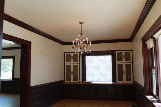 unfurnished dining area with an inviting chandelier, crown molding, wood finished floors, and wainscoting