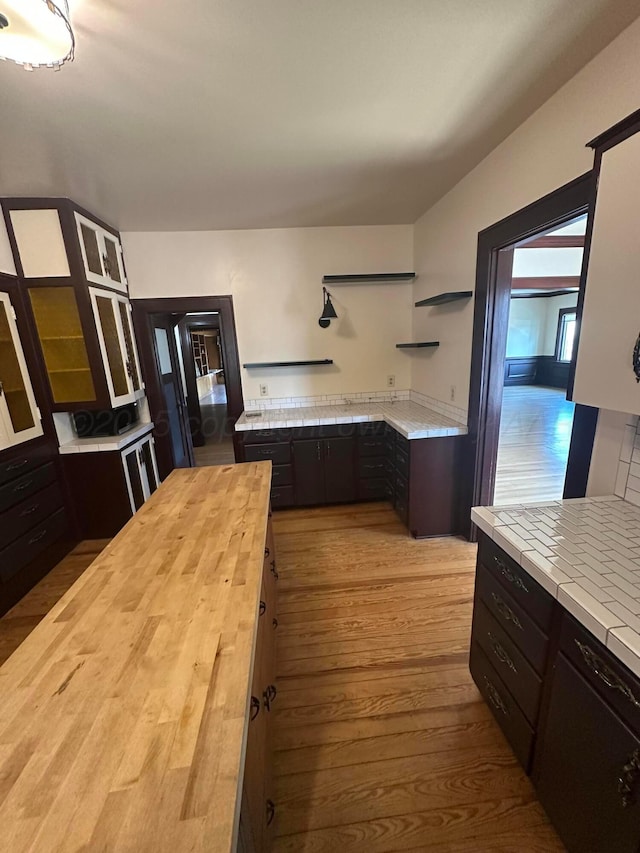 kitchen featuring dark brown cabinetry, butcher block counters, wood finished floors, and open shelves