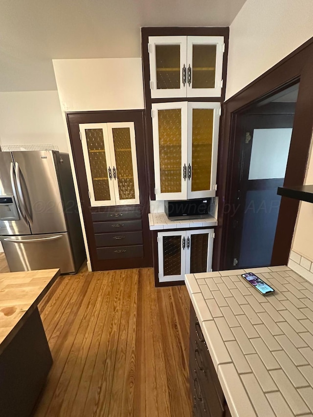 kitchen featuring tile counters, glass insert cabinets, wood finished floors, and stainless steel fridge