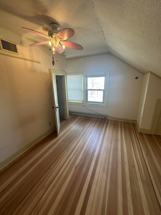 additional living space with visible vents, vaulted ceiling, light wood-style floors, a textured ceiling, and a baseboard heating unit