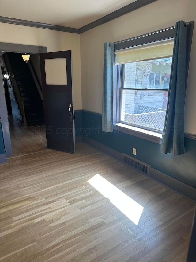 empty room with visible vents, light wood-style flooring, and ornamental molding
