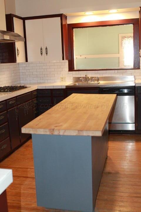 kitchen featuring butcher block countertops, under cabinet range hood, a sink, stainless steel dishwasher, and wood finished floors