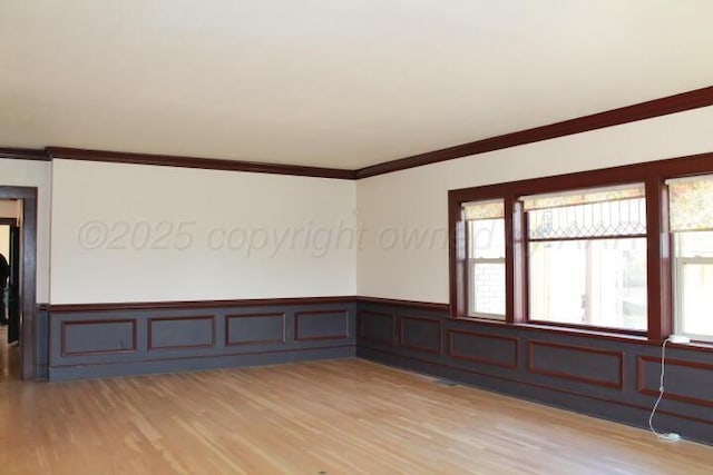 empty room with light wood finished floors, wainscoting, and ornamental molding