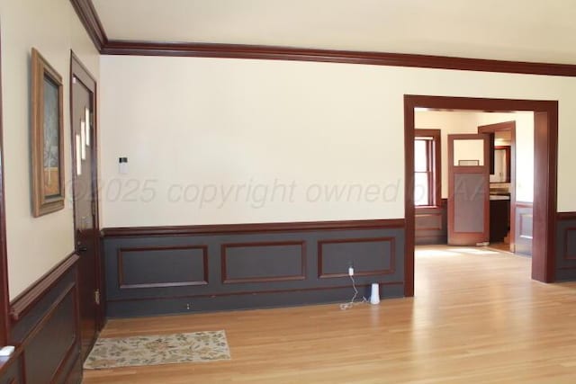 unfurnished room with a wainscoted wall, ornamental molding, and light wood-style flooring
