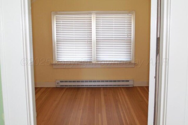 empty room featuring a baseboard radiator, baseboards, and wood finished floors