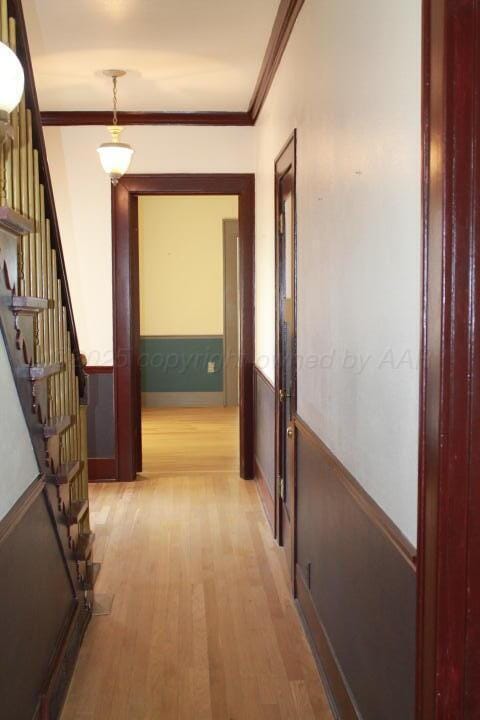 hallway with crown molding, light wood-style flooring, and stairway