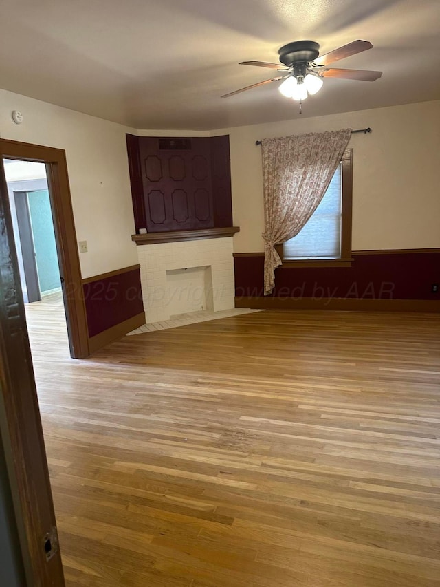 unfurnished room featuring a wainscoted wall, a fireplace, ceiling fan, and wood finished floors