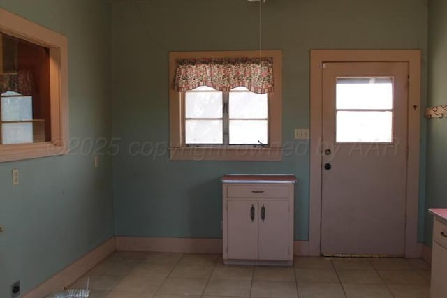 doorway to outside with light tile patterned floors, a healthy amount of sunlight, and baseboards