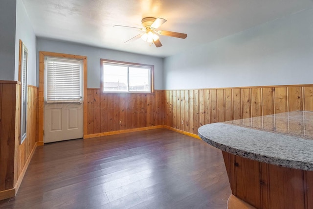 interior space featuring ceiling fan, dark wood-type flooring, and wooden walls