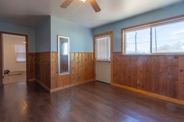 empty room featuring ceiling fan, plenty of natural light, dark wood-type flooring, and wood walls