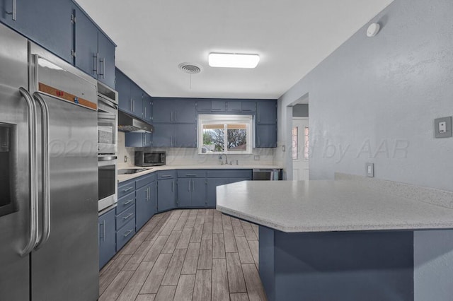 3412 Sunlite St, Amarillo, TX 79109 - kitchen featuring stainless steel appliances, blue cabinetry, under cabinet range hood, decorative backsplash, and light countertops