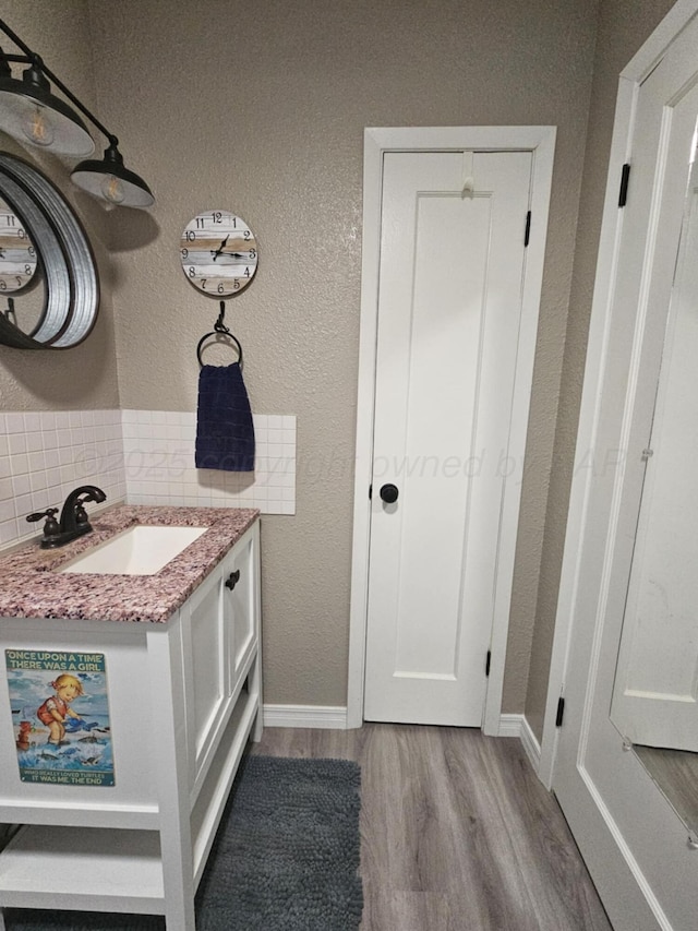 bathroom with baseboards, vanity, a textured wall, and wood finished floors