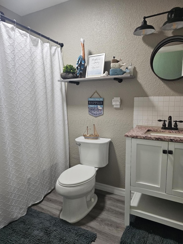 full bath with toilet, wood finished floors, vanity, and a textured wall