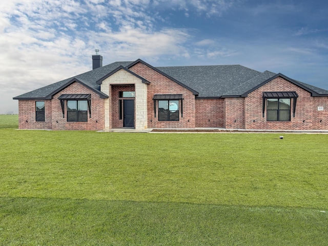 view of front of home with a chimney, brick siding, roof with shingles, and a front yard