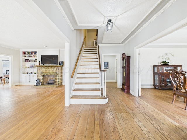 interior space with a textured ceiling, ornamental molding, light wood finished floors, a brick fireplace, and stairs