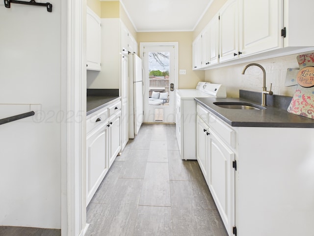 laundry area featuring separate washer and dryer, light wood-style flooring, cabinet space, a sink, and crown molding