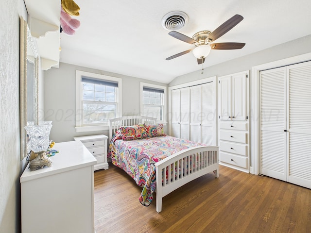 bedroom with ceiling fan, two closets, wood finished floors, visible vents, and lofted ceiling