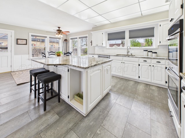 kitchen featuring light stone countertops, a breakfast bar area, stainless steel appliances, white cabinetry, and a center island