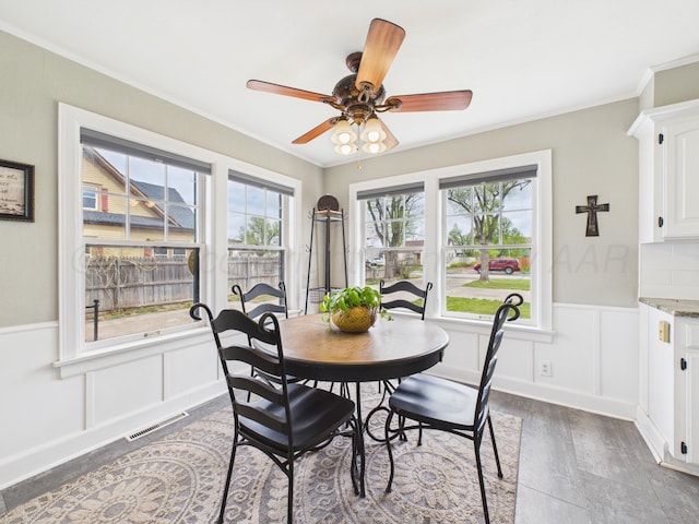 dining room with visible vents, dark wood-style flooring, ornamental molding, a ceiling fan, and wainscoting