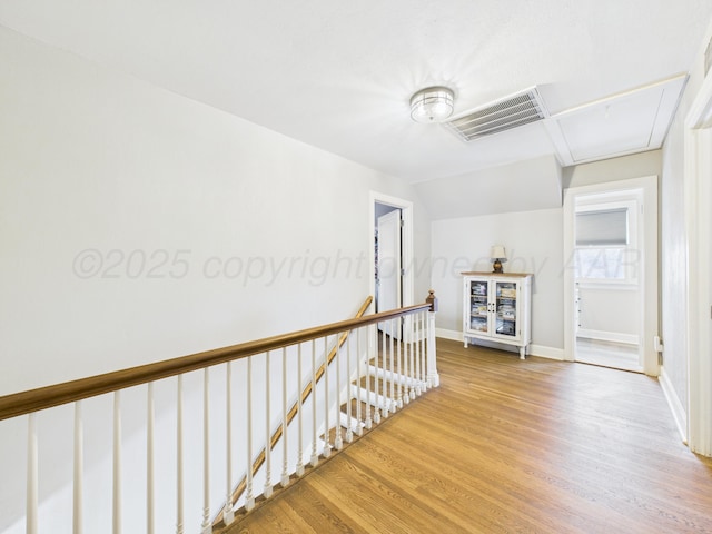 hall with wood finished floors, attic access, an upstairs landing, baseboards, and visible vents