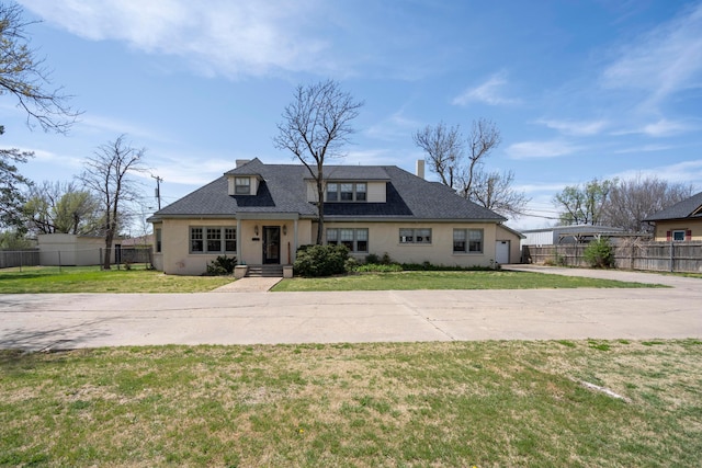 bungalow-style home with a front yard, driveway, stucco siding, and fence