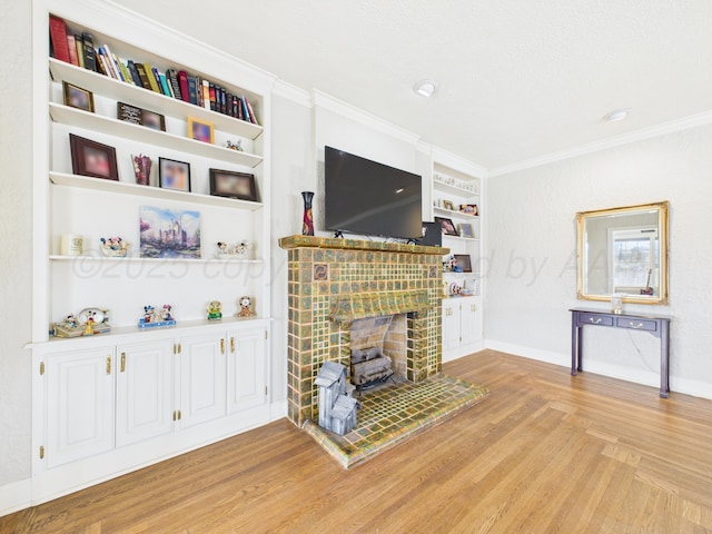 living area featuring ornamental molding, a brick fireplace, built in features, and light wood-type flooring