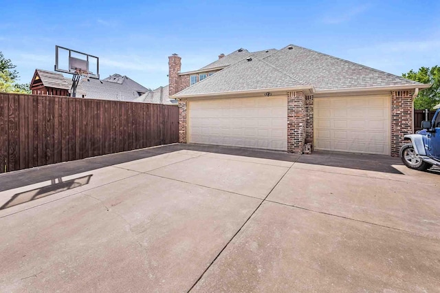 view of home's exterior with concrete driveway, brick siding, a shingled roof, and fence