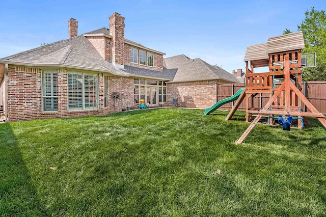 rear view of house featuring a lawn, a chimney, brick siding, fence, and a playground