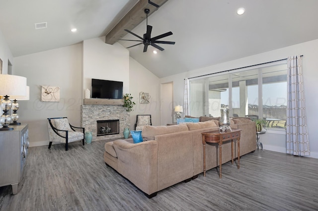 living room featuring beamed ceiling, a stone fireplace, a ceiling fan, and wood finished floors