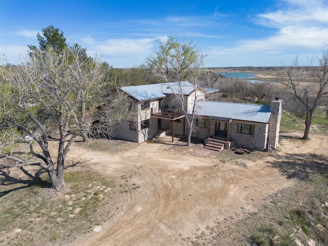 view of front facade with a water view, metal roof, stone siding, and a chimney