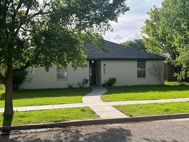 single story home featuring a front yard, a shingled roof, and brick siding