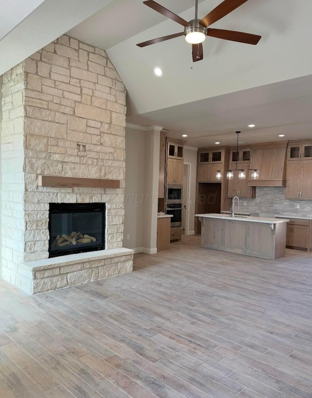 unfurnished living room featuring sink, vaulted ceiling, light wood-type flooring, ceiling fan, and a fireplace
