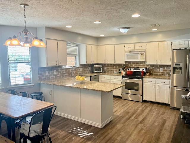 kitchen featuring a peninsula, white cabinetry, appliances with stainless steel finishes, and dark wood-style flooring
