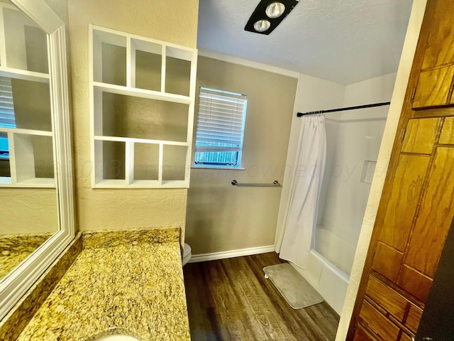 bathroom featuring baseboards, a textured wall, wood finished floors, and shower / bathtub combination with curtain