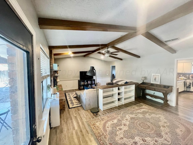 living room featuring a ceiling fan, a textured ceiling, lofted ceiling with beams, light wood-style flooring, and visible vents