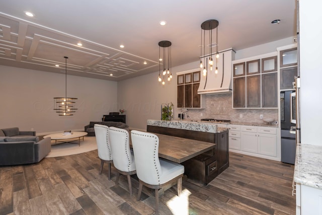 kitchen with open floor plan, glass insert cabinets, premium range hood, backsplash, and dark wood-style floors