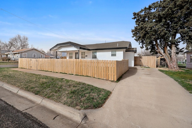 bungalow featuring a fenced front yard, concrete driveway, and roof with shingles
