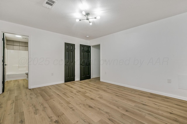 unfurnished bedroom with a notable chandelier, baseboards, visible vents, and light wood finished floors