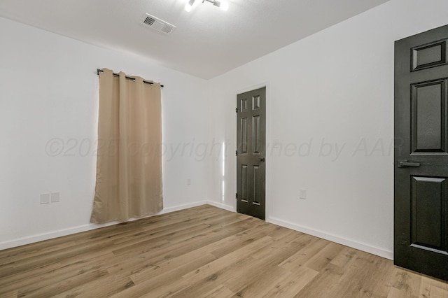 unfurnished room with light wood finished floors, visible vents, and baseboards