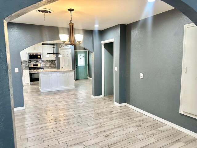 kitchen with pendant lighting, appliances with stainless steel finishes, white cabinets, decorative backsplash, and light wood-type flooring