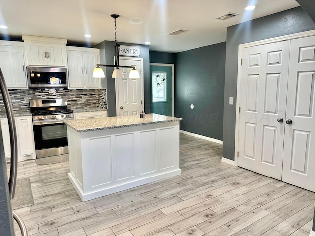 kitchen featuring appliances with stainless steel finishes, a kitchen island, pendant lighting, light stone countertops, and white cabinets