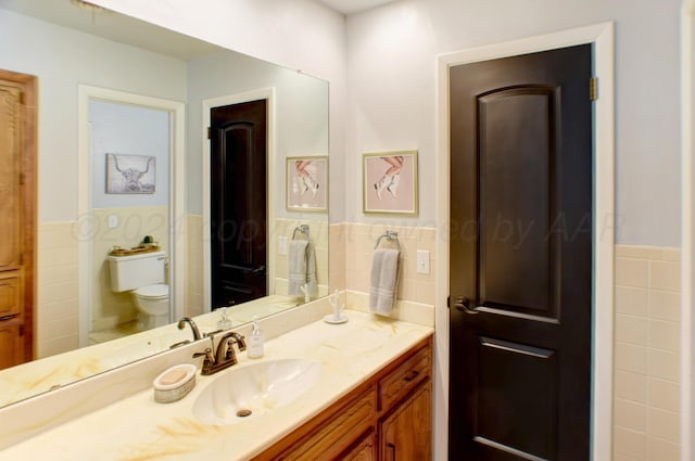 bathroom with toilet, vanity, and tile walls