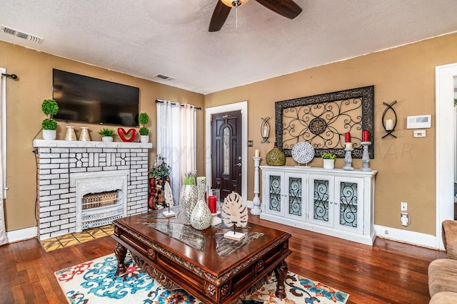 living room with a fireplace, dark hardwood / wood-style floors, a textured ceiling, and ceiling fan