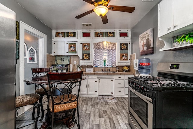 kitchen with light wood-type flooring, appliances with stainless steel finishes, sink, white cabinets, and ceiling fan