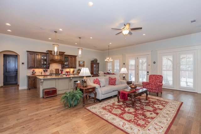 living room featuring light wood-type flooring, ceiling fan with notable chandelier, and crown molding